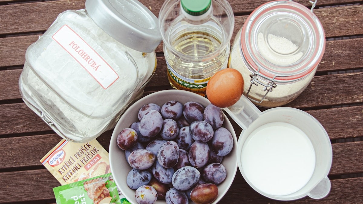 a bowl of plums, eggs, milk, and other ingredients on a table